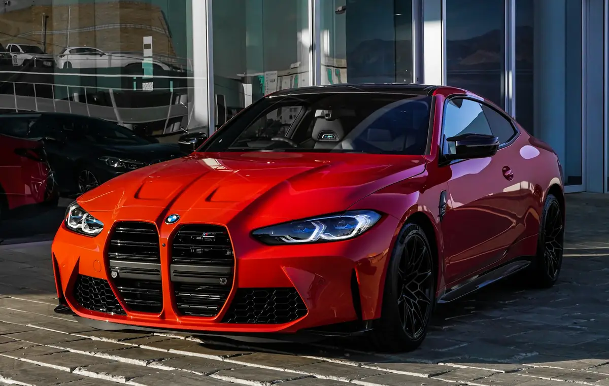 Red BMW M4 Competition in hard light outside a dealership glass front