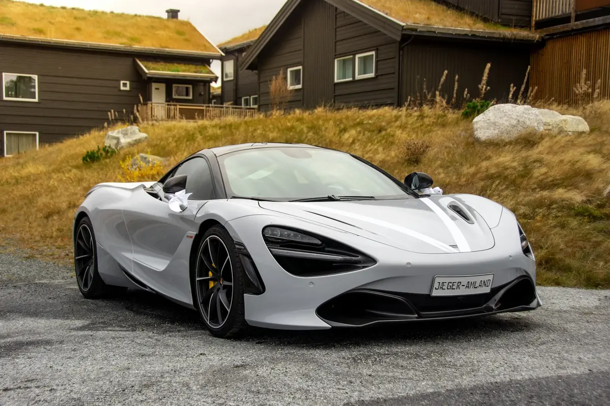 Grey McLaren 720S, three-quarter front view by autumn hillside cabins